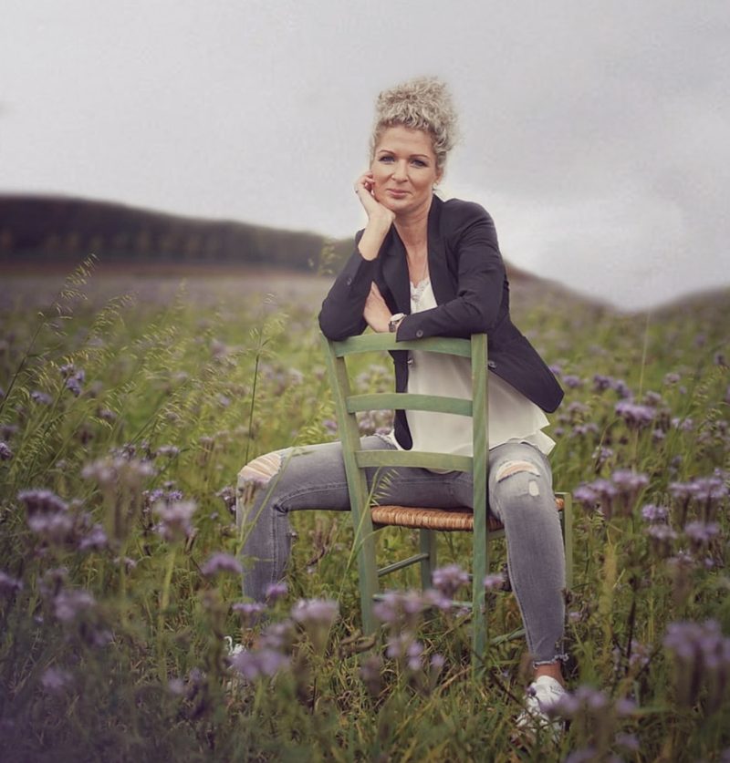Carina sitzt auf einem grünen Stuhl in einem Blumenfeld